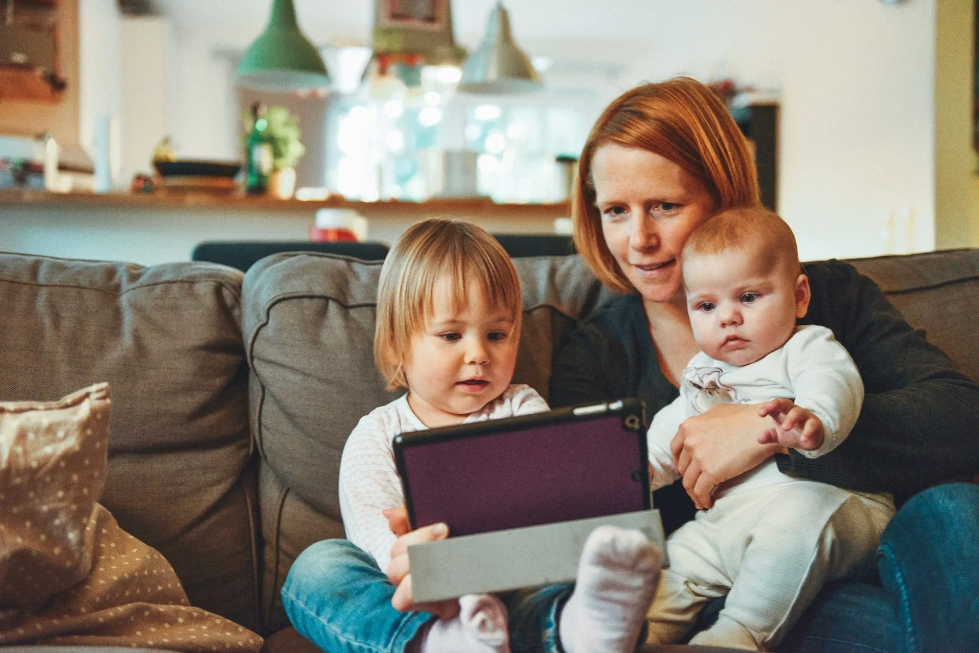 A mother on the couch with a baby and a toddler
